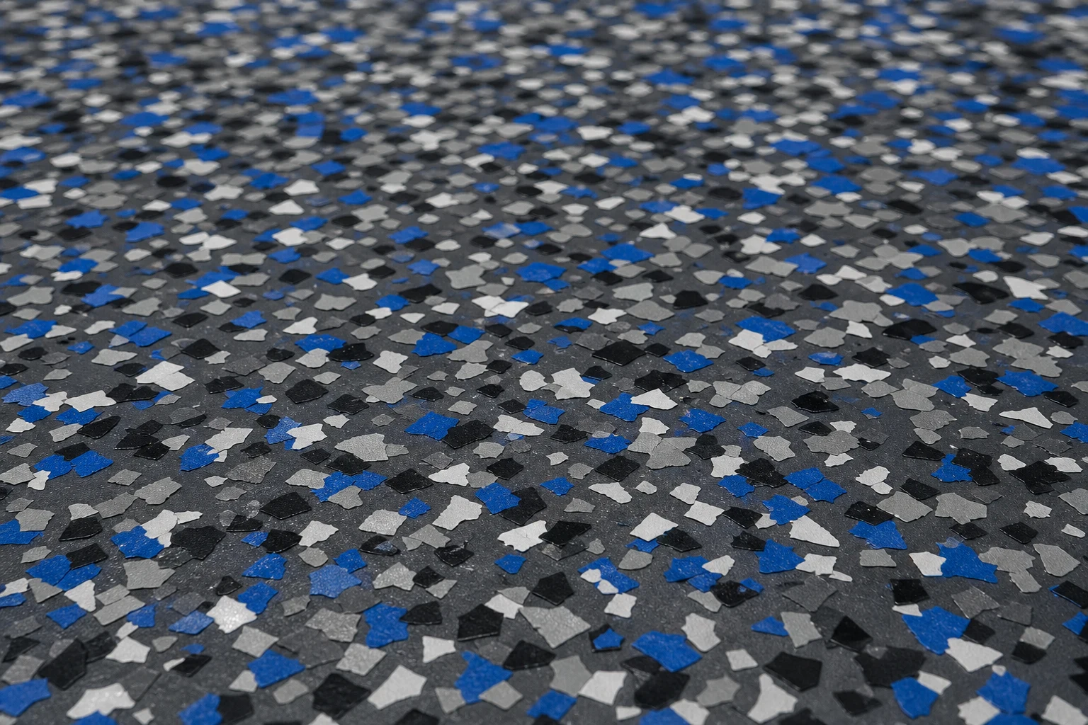 Decorative vinyl colour flakes scattered densely across a freshly coated charcoal epoxy floor before the clear sealer is applied