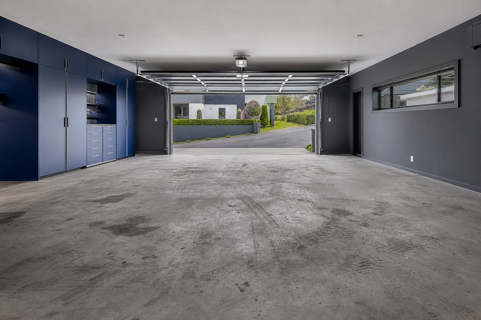 Bare grey concrete double garage slab before coating, showing oil staining, tyre marks, dust and fine surface cracks