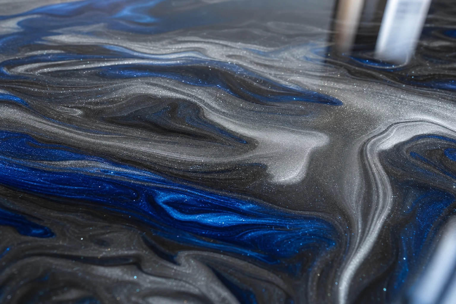 Extreme close-up of a metallic epoxy surface showing layers of silver and cobalt pigment suspended under a thick glass-like clear coat